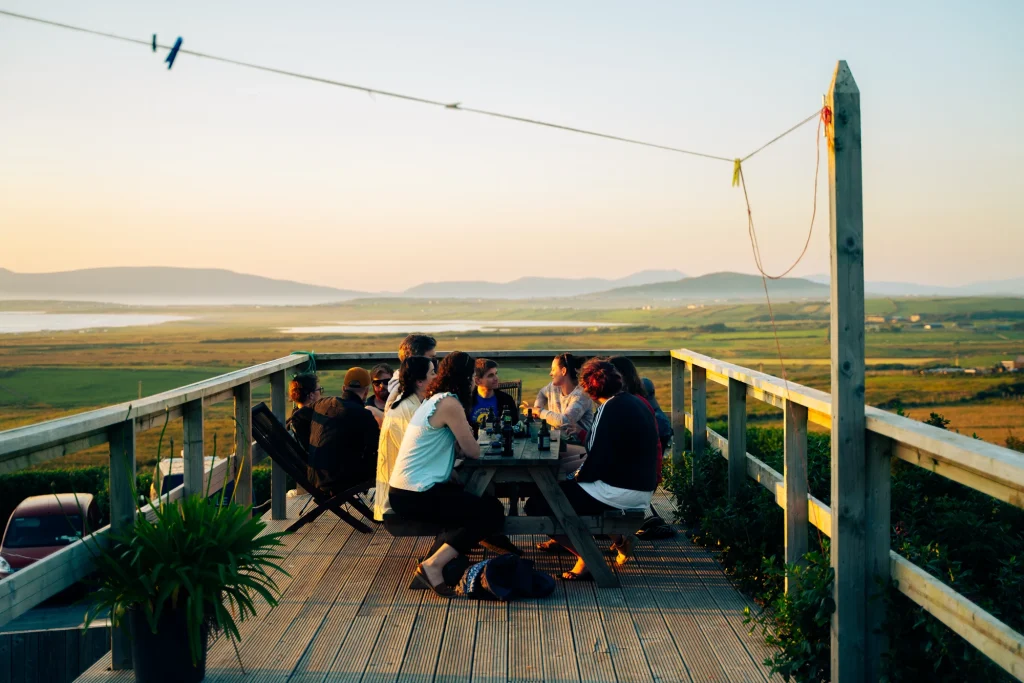 Group dining on a wooden deck, overlooking scenic Irish countryside at sunset.