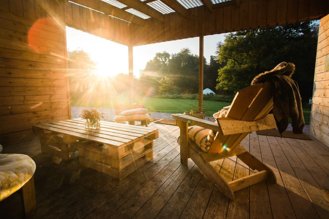 Cosy wooden deck at sunset with chairs and table, overlooking lush garden; serene outdoor retreat setting.