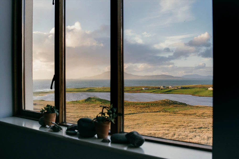 Scenic coastal view from window, showing Irish countryside, ocean, clouds, and small houses.