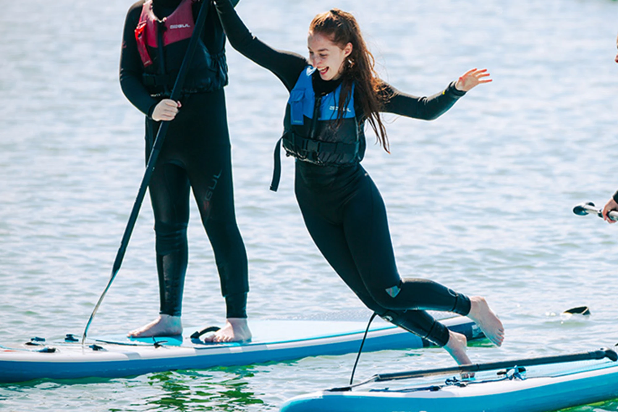 Woman in wetsuit joyfully falling off paddleboard into water. Paddleboarding adventure, summer activity.