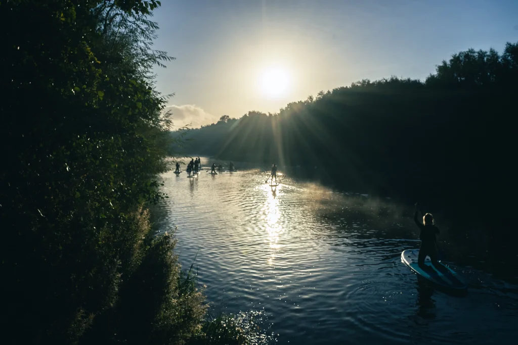 Paddleboarders on a tranquil river at sunrise, surrounded by lush greenery.