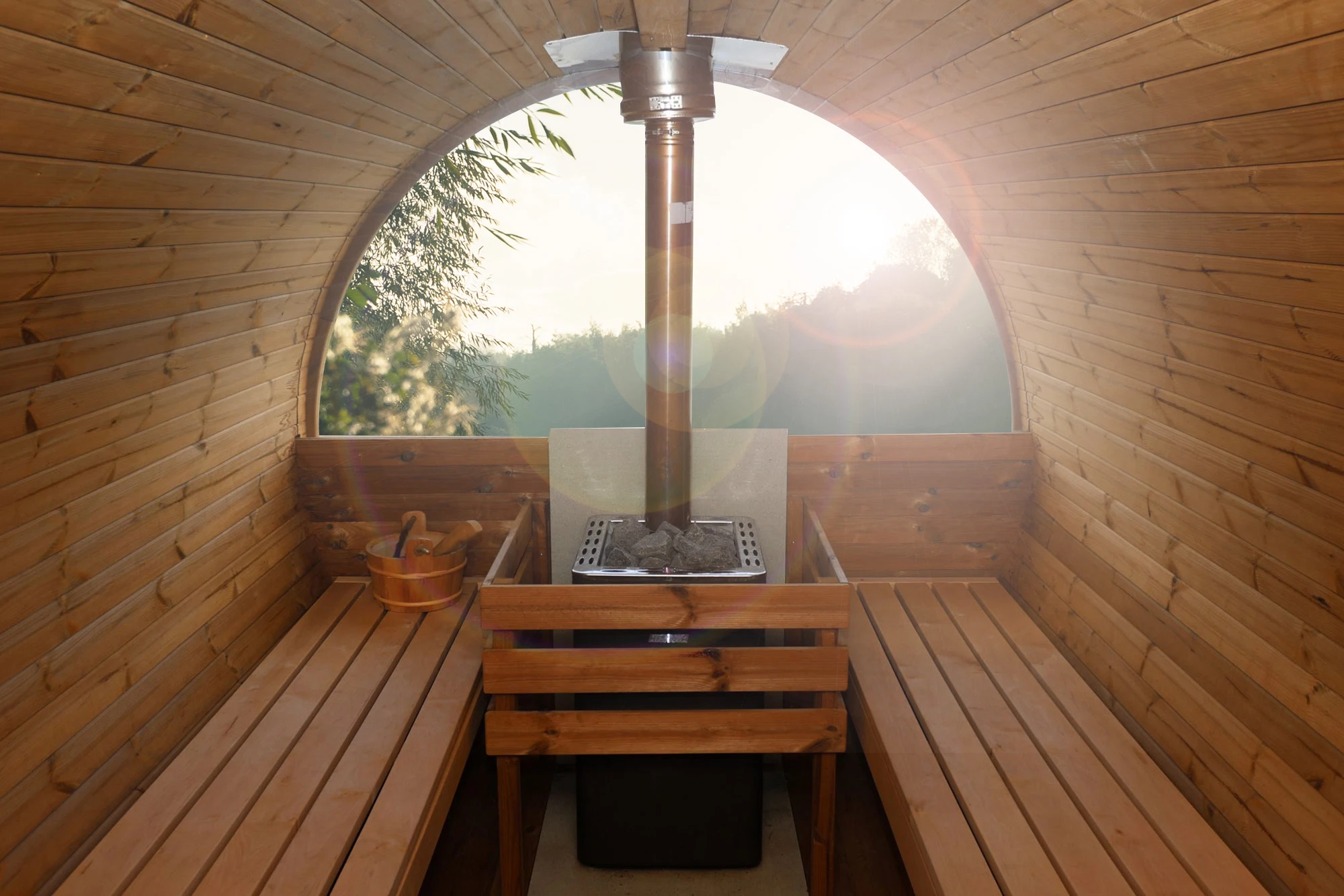 Wooden barrel sauna interior with sunlight through window, featuring benches and a central stove.