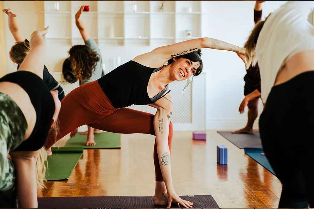 Women practising yoga in a bright studio, performing side stretches on mats.