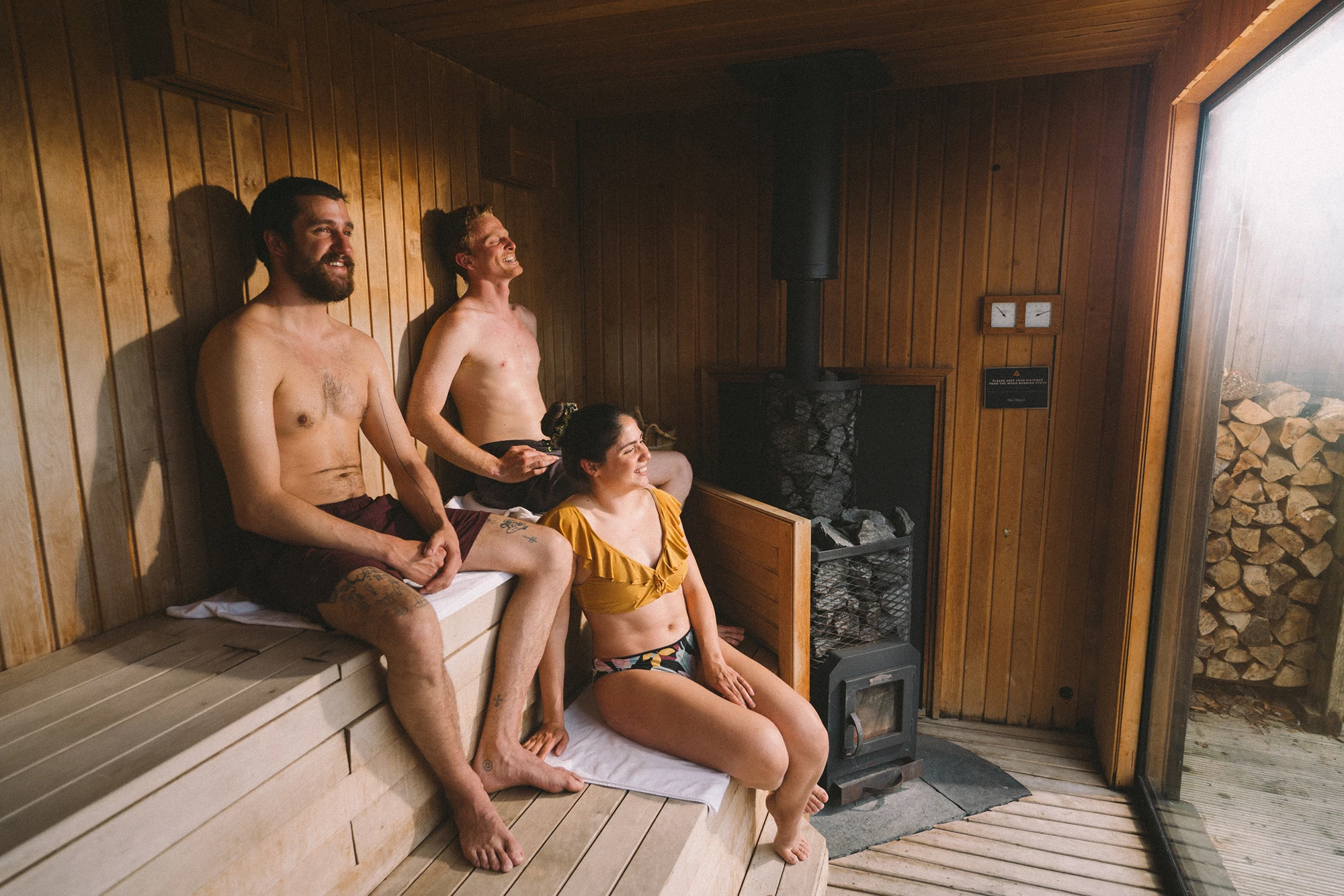 Three people relaxing in a wooden sauna, enjoying the warmth from the stove.