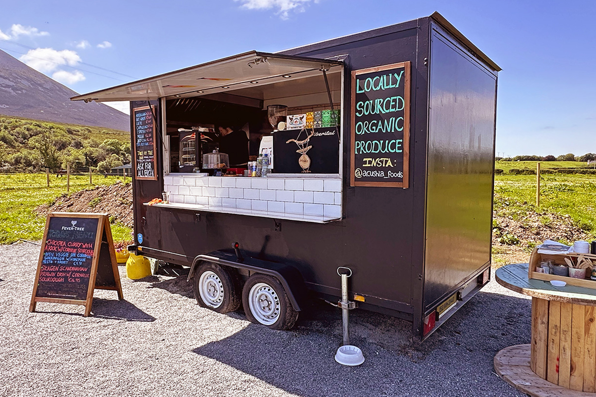 Food truck serving locally sourced organic produce, with menu board, set in a scenic rural location.