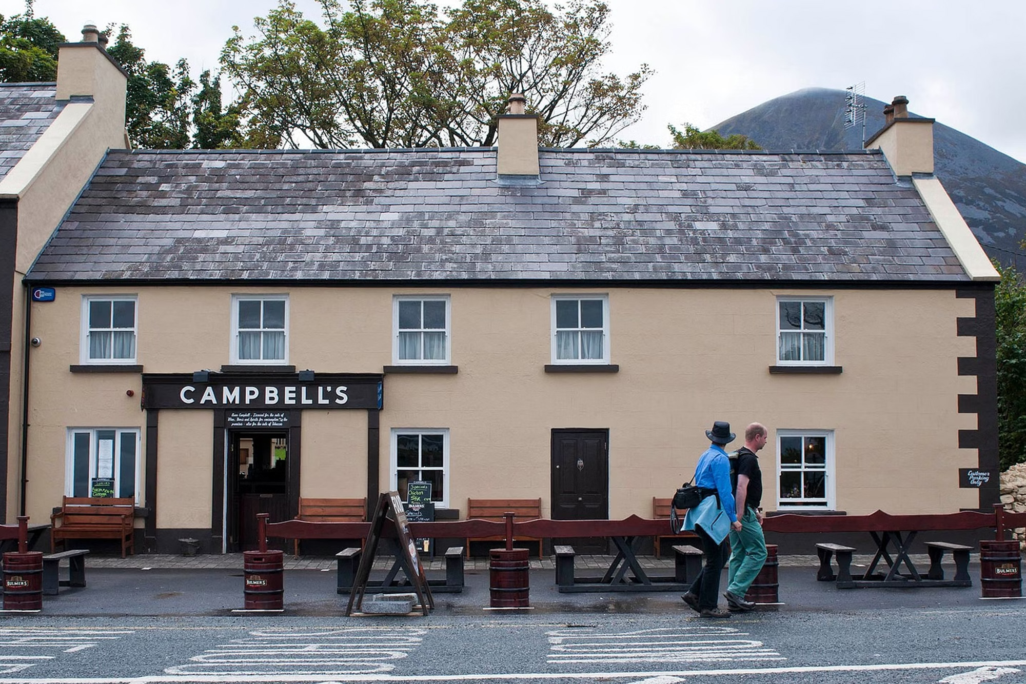 Historic Campbell's pub in Ireland with slate roof; two men walking past on a quiet street.