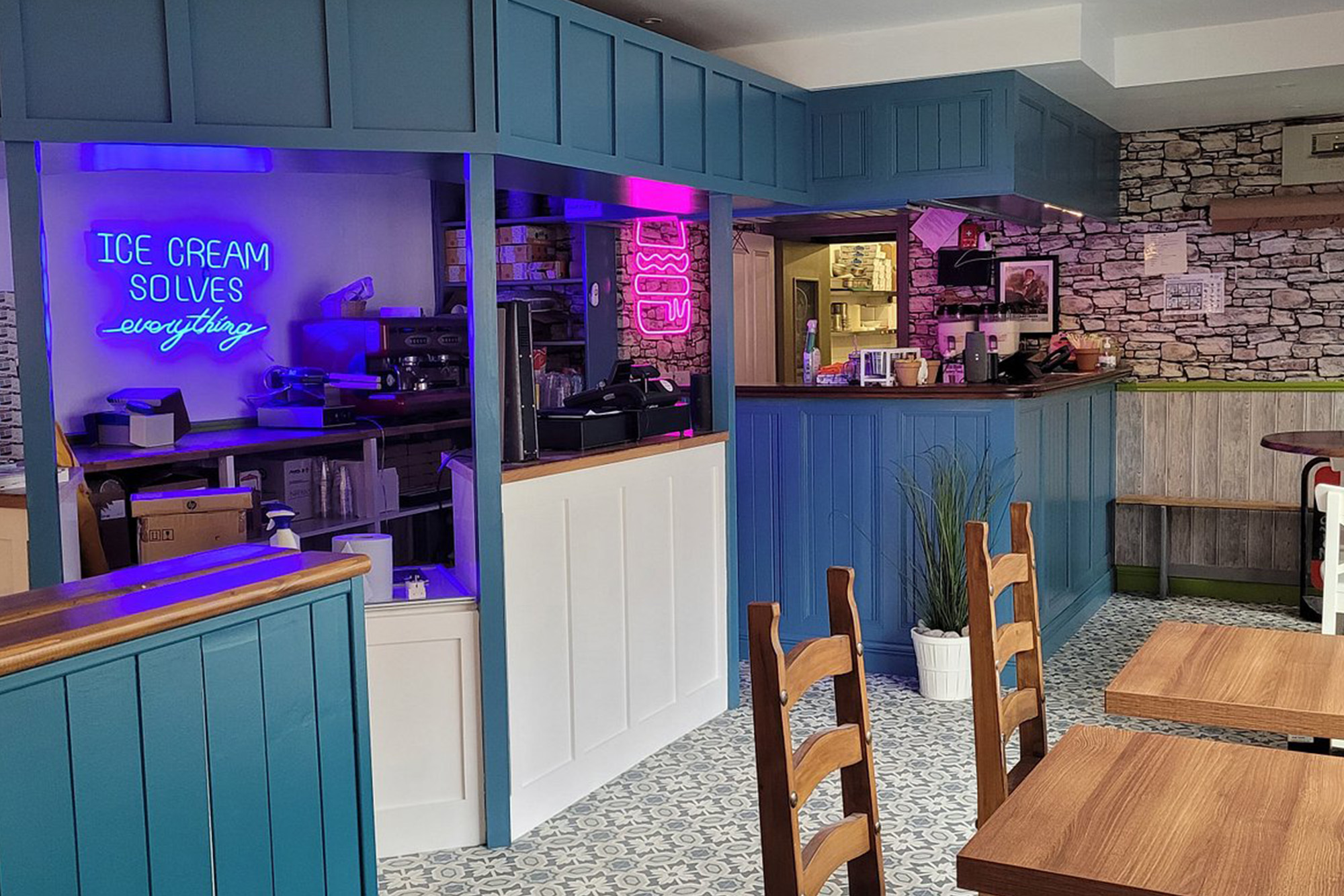 Cosy ice cream parlour interior with blue decor, rustic tables, neon sign saying Ice Cream Solves Everything.